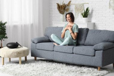 Evdeki kanepede oturmuş meditasyon yapan genç bir kadın.