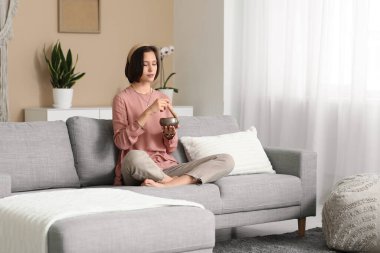 Tibet şarkı kasesi olan genç bir kadın evdeki kanepede otururken meditasyon yapıyor.