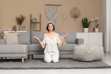 Genç bir kadın evde yerde oturmuş meditasyon yapıyor.