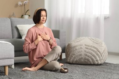 Genç bir kadın evde yerde oturmuş meditasyon yapıyor.