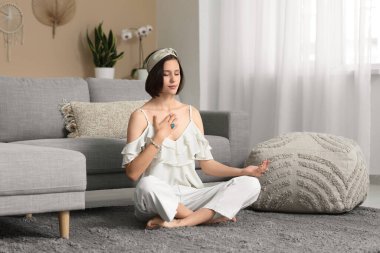 Genç bir kadın evde yerde oturmuş meditasyon yapıyor.