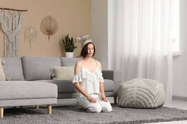 Genç bir kadın evde yerde oturmuş meditasyon yapıyor.
