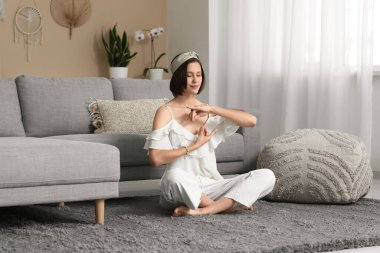 Genç bir kadın evde yerde oturmuş meditasyon yapıyor.