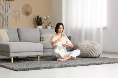 Evde yerde oturmuş meditasyon yapan genç bir kadın.