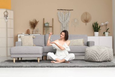 Evde yerde oturmuş meditasyon yapan genç bir kadın.