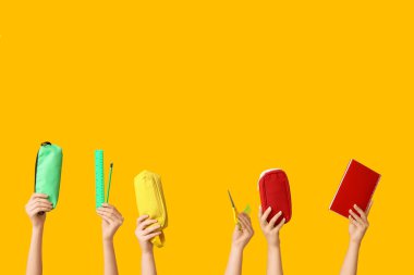 Sarı zemin üzerinde kalem, defter, makas, cetvel ve kalem bulunan kadın elleri