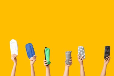 Sarı arka planda farklı kalem kılıfları olan kadın eller.