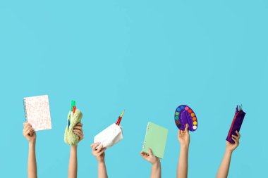 Boya paletli kadın elleri, not defterleri ve mavi zemin kaplamalı kalem kılıfları.