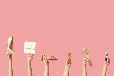 Çantalı kadın elleri, farklı güneş gözlükleri ve pembe arka planda topuklu ayakkabılar.