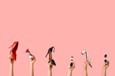 Farklı güneş gözlüklü kadın elleri ve pembe arka planda topuklu ayakkabılar.