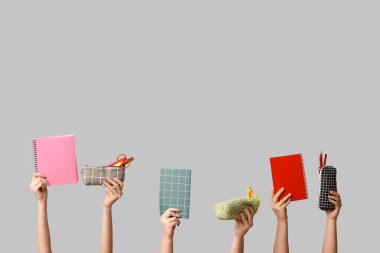 Gri arkaplanda kırtasiyeli defter ve kalem kılıfları tutan kadın eller