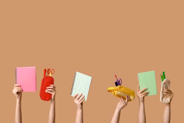 Bej arka planda kırtasiyeli not defterleri ve kalem kılıfları tutan kadın eller