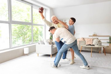 Dede ve babasıyla evde rugby oynayan genç bir çocuk.