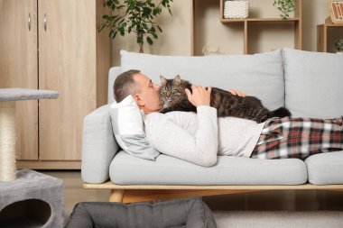 Evdeki kanepede tatlı kedisi olan olgun bir adam yatıyor.