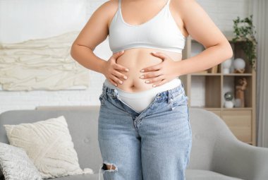 Şişman, genç bir kadın evinde aynanın yanında karnına dokunuyor, yakın plan. Kilo alma kavramı