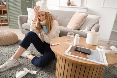 Sıcak su şişesiyle evde oturan hasta genç bir kadın.