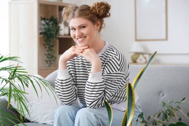 Evdeki kanepede oturan yeşil çiçekli genç kadın.