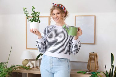 Sulama kabı olan ve evde bitki yetiştiren genç bir kadın.