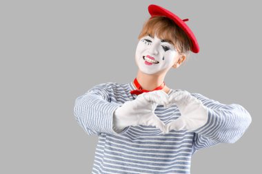 Kadın pandomimist elleri gri arka planda kalp yapıyor.