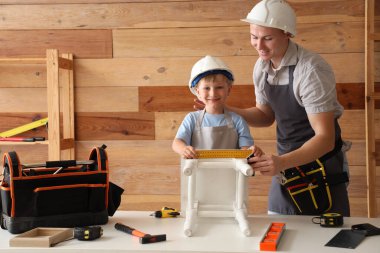 Küçük oğlu ile birlikte atölyede tabure montajlayan bir erkek işçi.