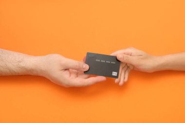 Turuncu arka planda kredi kartı olan sevgi dolu genç bir çiftin elleri.