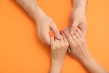 Turuncu arka planda nişan yüzüğü takan genç çiftin elleri.