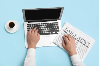 Dizüstü bilgisayarı, gazetesi ve mavi arka planda bir fincan kahvesi olan erkek eller.
