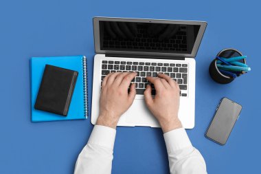 Mavi arka planda dizüstü bilgisayarı, defterleri ve cep telefonu olan erkek eller