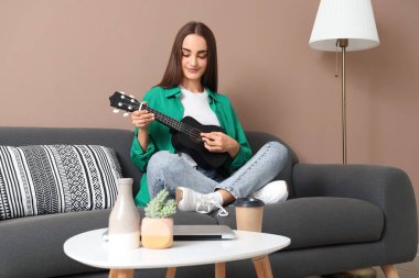 Evdeki kanepede gitar çalan genç ve güzel bir kadın.