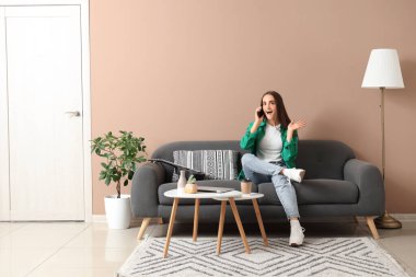 Evdeki koltukta cep telefonuyla konuşan genç ve güzel bir kadın.