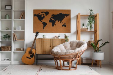 Rahat koltuk, çekmeceler, gitar ve dünya haritası oturma odasının iç tarafındaki beyaz duvarda.