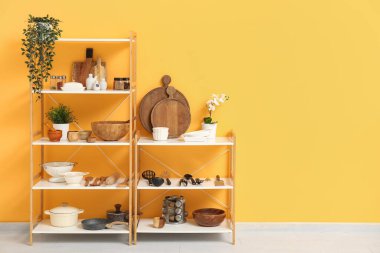 Mutfakta sarı duvarın yanında mutfak aletleri olan modern raf ünitesi.