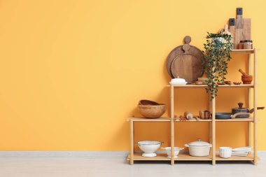 Mutfakta sarı duvarın yanında bulaşık takımı olan modern raf ünitesi.