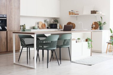 Beyaz duvarın yanında masalı, sandalyeli ve tezgahlı bir yemek odası.