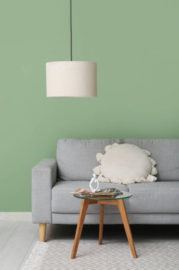 Asılı lamba, rahat bir kanepe ve içinde insan figürü ve dergi olan bir sehpa.