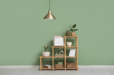 Sallanan lamba ve raf ünitesi, yeşil duvarın yanında çiçekler var.