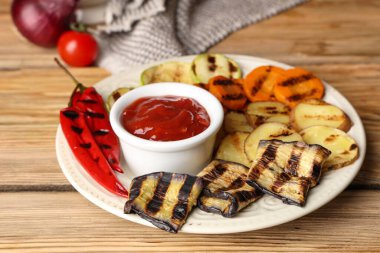 Izgara sebzeli tabak ve ahşap kaplama soslu kase, yakın plan.