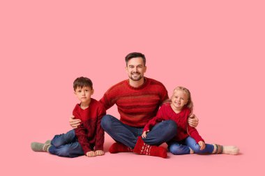 Mutlu ve çocuklu bir baba pembe arka planda oturuyor.