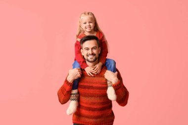 Mutlu baba ve kızı pembe arka planda kışlık giysiler içinde.