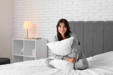 Genç ve güzel bir kadın evde yastıkla sarılıyor.