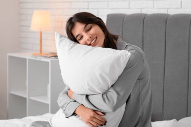 Genç ve güzel bir kadın evde yastıkla sarılıyor.