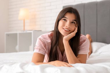 Genç ve güzel bir kadın evde yatakta yatıyor.