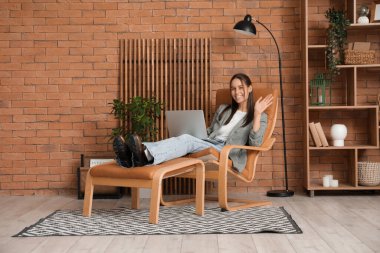 Genç bir kadın koltuğunda oturuyor ve evinde dizüstü bilgisayar kullanıyor.