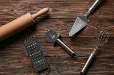 Ahşap arka planda paslanmaz çelik pizza keskisi olan farklı mutfak aletleri.