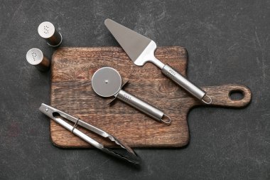 Ahşap tahta tahta, paslanmaz çelik pizza kesici, spatula, maşa ve baharatlar.