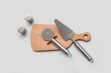 Çelik spatulalı ahşap tahta, pizza bıçağı ve gri arka planda baharatlar.