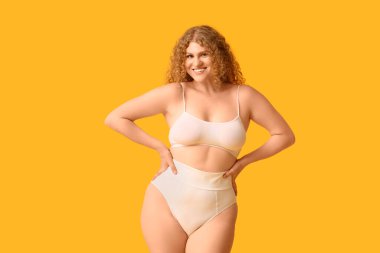 Güzel, genç, mutlu, pozitif kadın sarı arka planda moda iç çamaşırlı.