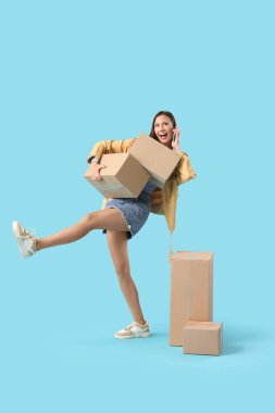 Mavi arka planda cep telefonuyla konuşan güzel, mutlu, genç bir kadın.