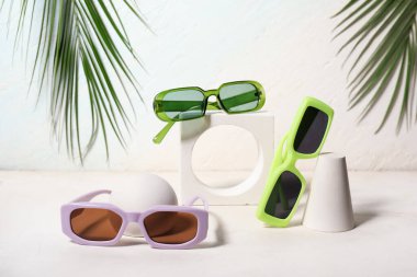 Beyaz arkaplanda farklı güneş gözlükleri ve palmiye yaprakları