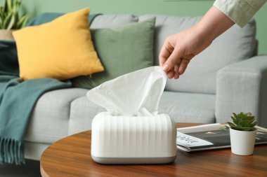 Oturma odasındaki sehpadan kağıt mendil alan kadın.